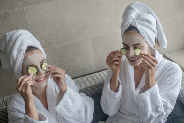 Młode kobiety z ręcznikiem na głowach nakładające plastry ogórka na oczy — Zdjęcie stockowe