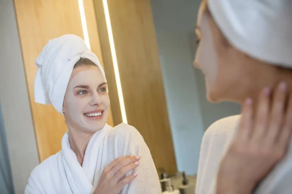 Jeune femme avec masque facial regardant dans le miroir — Photo