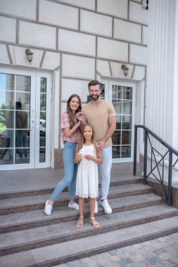 Genç bir aile merdivenlerde durup gülümsüyor.