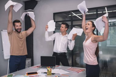 Heyecanlı kadın ve iki erkek iş arkadaşı gülüyor, kağıtları fırlatıyor.