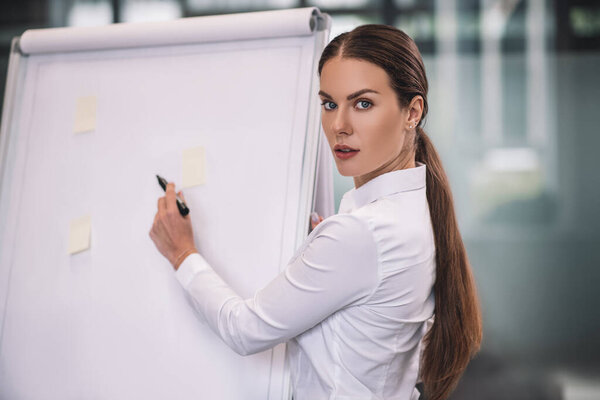 Brown-haired businesswoman in white shirt writing on flipchart with left hand