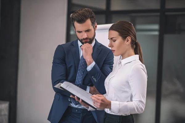 Braunhaarige Frau mit bärtigem männlichen Kollegen beim Vorlesen von Zeitungen — Stockfoto