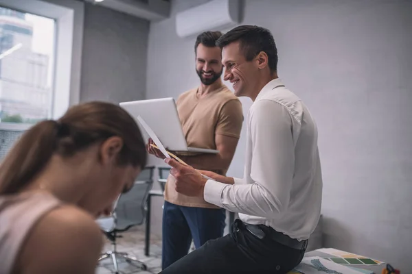 Varón barbudo con portátil hablando con su compañero de trabajo, ambos sonriendo — Foto de Stock