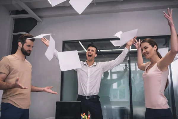 Glad kvinna och två manliga medarbetare kastar papper — Stockfoto