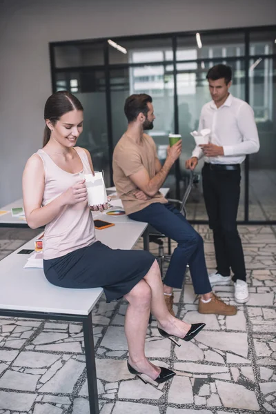 Smiling dark-haired female sitting on table, opening chinese food box