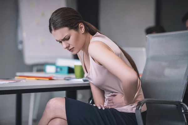 Wanita berambut coklat duduk di meja, membungkuk, menyentuh perutnya — Stok Foto