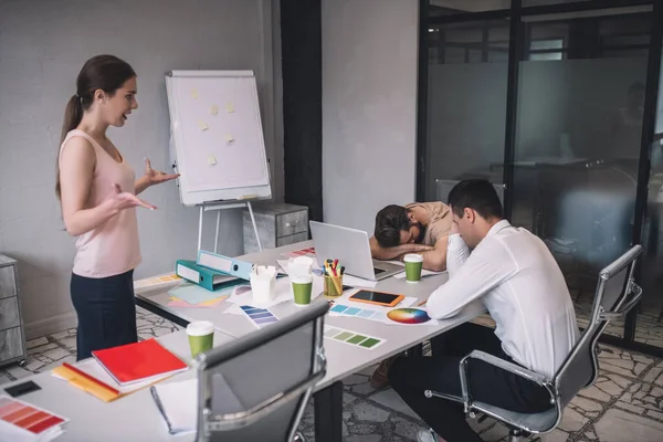 Mujer de cabello castaño hablando con un colega varón cansado, sentado en la mesa, apoyando la cabeza en las manos — Foto de Stock