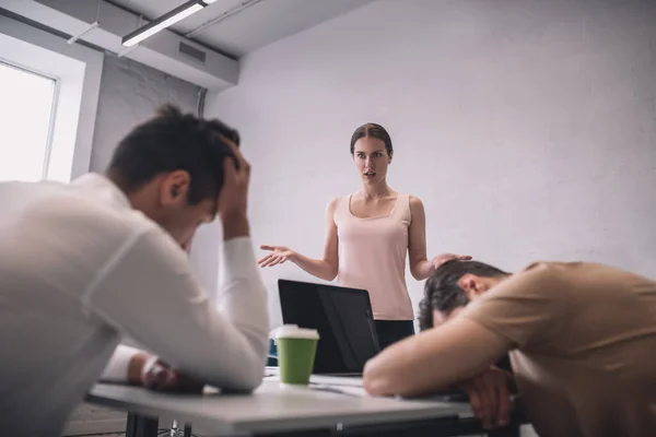 Mujer de cabello castaño de pie delante de un colega varón cansado — Foto de Stock