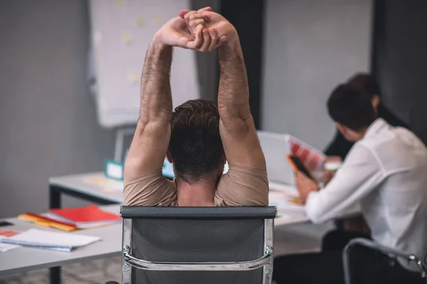 Back view of dark-haired male sitting at meeting, stretching — Stock Photo, Image