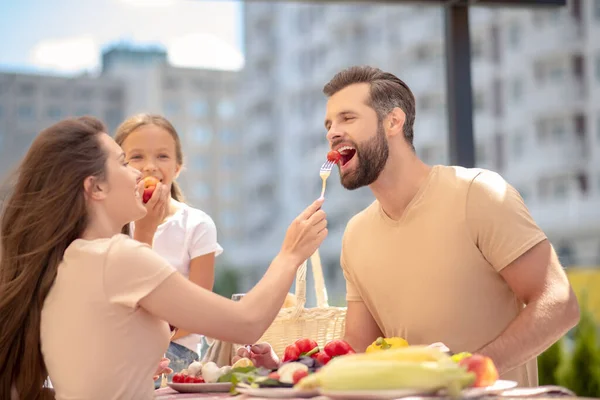 Joven esposa alimentando a su marido con tomate y riendo — Foto de Stock