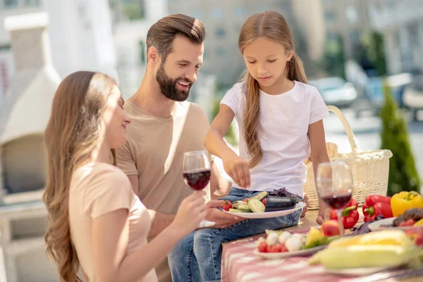 Genç, şirin bir aile dışarıda yemek yiyor ve neşeli görünüyor. — Stok fotoğraf