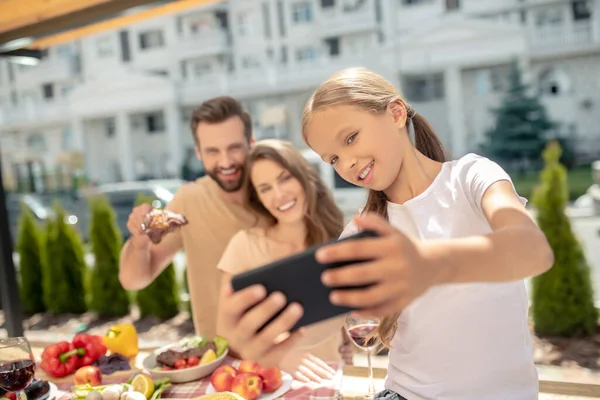 Menina de cabelos claros em tshirt branca fazendo selfie com os pais — Fotografia de Stock