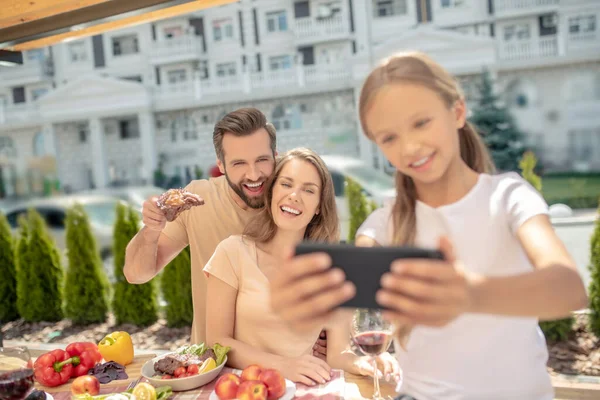 Menina de cabelos claros em tshirt branca fazendo selfie com pais felizes — Fotografia de Stock