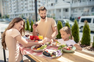 Genç bir aile dışarıda yemek yiyor ve mutlu görünüyor.