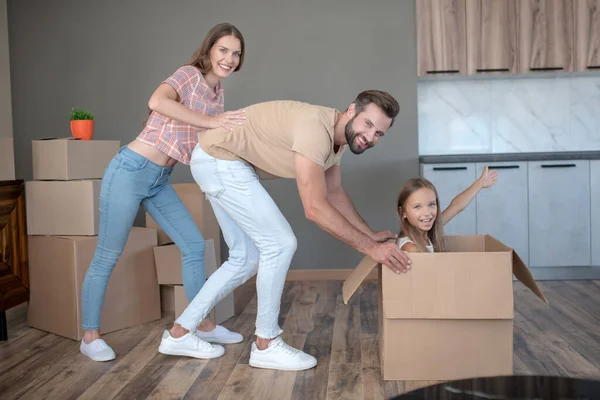 Linda chica sentada en una caja y divirtiéndose con sus padres —  Fotos de Stock