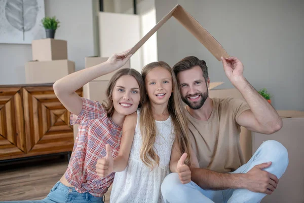 Семья сидит под крышей бумаги и чувствует себя счастливым — стоковое фото