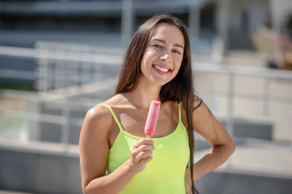 Ciemnowłosa dziewczyna w żółtym top uśmiecha się i trzyma lody — Zdjęcie stockowe