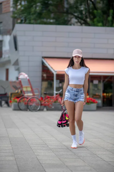 Pretty girl in shorts and top walking with roller-skates in hands — Stock Photo, Image
