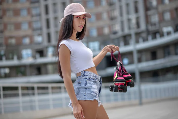 Fit girl in cap carrying roller-skates in hands