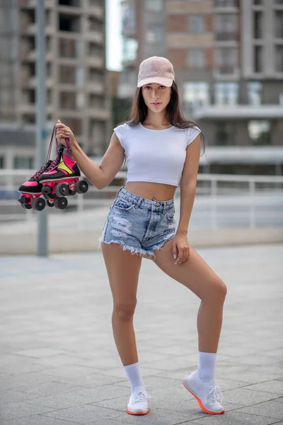 Fit Mädchen mit Mütze posiert mit Rollschuhen in der Hand — Stockfoto