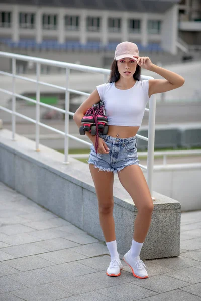 Pasvorm meisje in jeans shorts staan met rolschaatsen in handen — Stockfoto