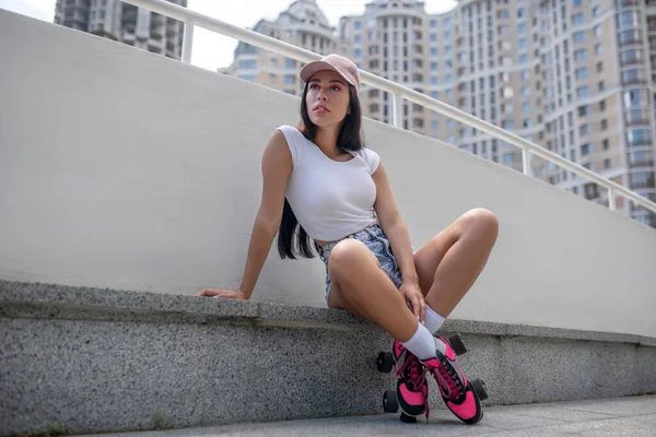 Menina em calções de ganga e em patins sentados no passeio de rua — Fotografia de Stock