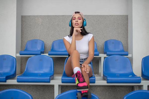 Donkerharig meisje in rolschaatsen die naar muziek luistert en er attent uitziet — Stockfoto