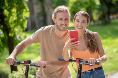 Genç, gülümseyen bir çift parkta selfie çekiyor.