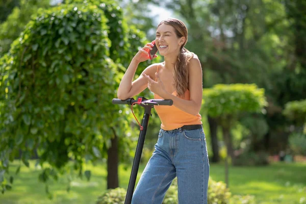 Young girl in orange top talking on the phone and feeling excited — Stock Photo, Image