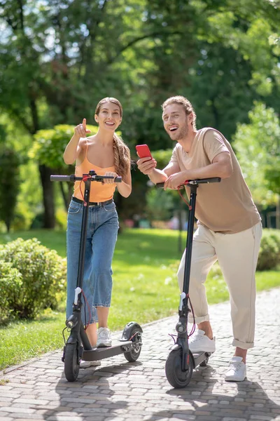 Jovem casal em scooters fazendo selfie no parque — Fotografia de Stock