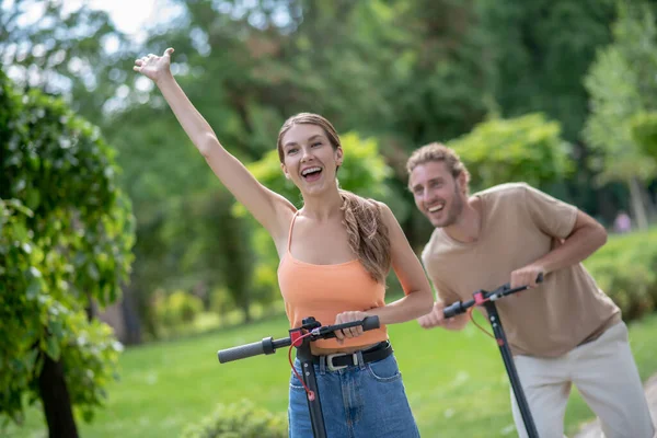 Fiatal pár lovaglás robogók a parkban, és látszó izgatott — Stock Fotó