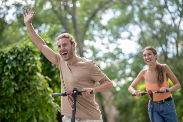 Pareja joven montando scooters en el parque y mirando feliz — Foto de Stock