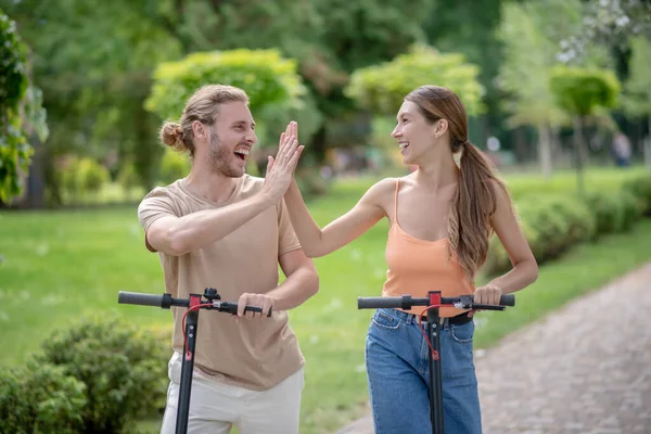 Молодая пара ездит на скутерах в парке и чувствует себя забавным — стоковое фото