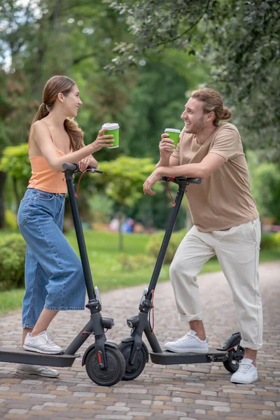 Jong stel met scooters aan het praten in het park en koffie drinken — Stockfoto