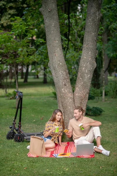 Jovem casal sentado debaixo da árvore e fazendo um piquenique — Fotografia de Stock