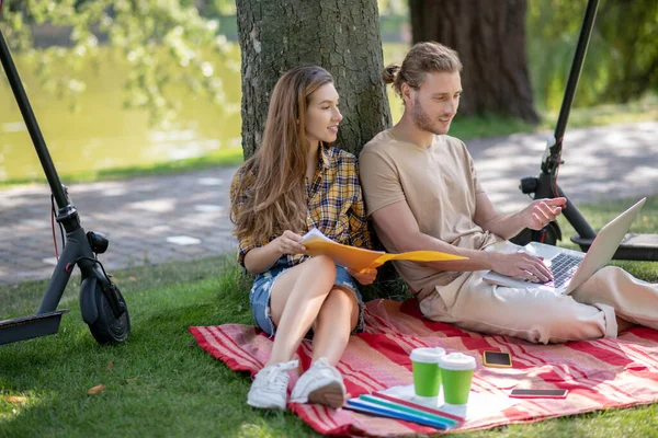 Two young people sitting under the tree and studying