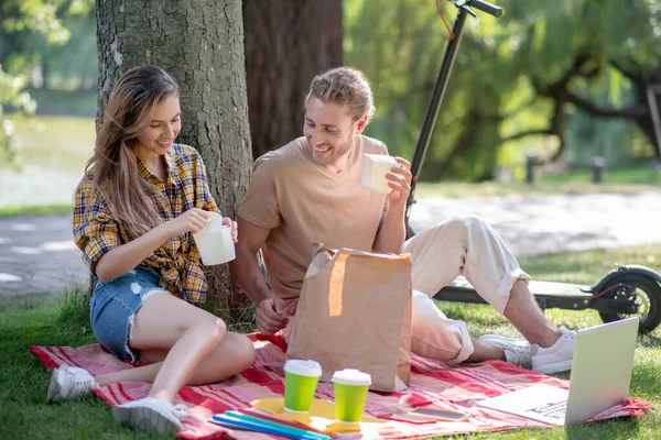 Pareja joven descansando en el parque y almorzando bajo el árbol —  Fotos de Stock