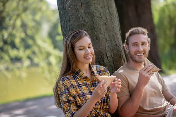 Unga par äter smörgåsar och ser nöjda ut — Stockfoto