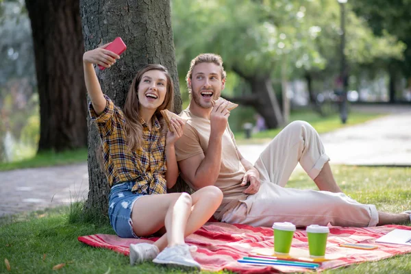 Jeune couple manger des sandwichs et faire du selfie — Photo