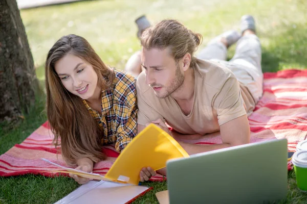 Pareja joven acostada en la hierba y estudiando —  Fotos de Stock