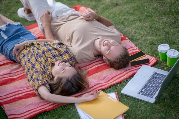 Joven pareja feliz tumbada en la hierba y relajándose después de estudiar —  Fotos de Stock