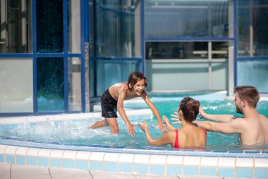 Yüzme havuzuna atlayan gülümseyen bir çocuk.