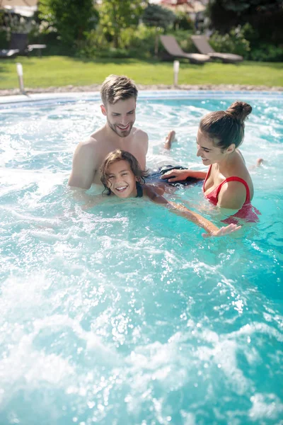 Des parents excités apprenant à leur fils souriant à nager dans la piscine — Photo