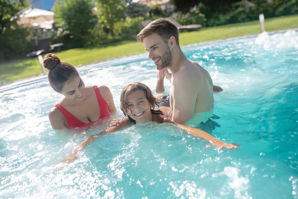 Emocionados padres enseñando a su hijo sonriente a nadar en la piscina — Foto de Stock