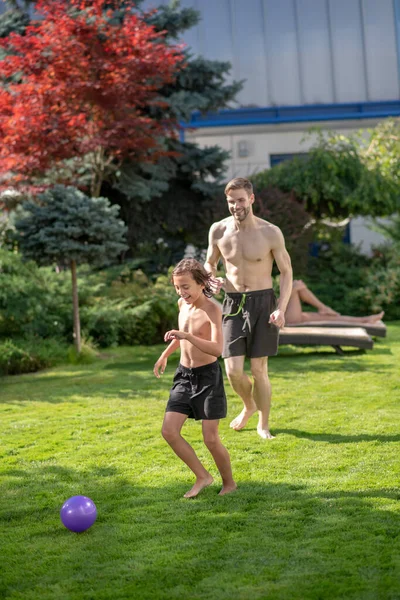 Alegre padre e hijo corriendo con pelota en el césped — Foto de Stock