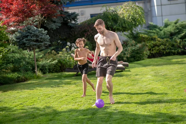 Baba ve oğul çimenlikte top peşinde koşuyorlar. — Stok fotoğraf