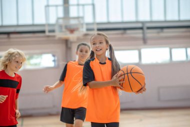 Parlak spor giyimli çocuklar basketbol oynuyorlar.