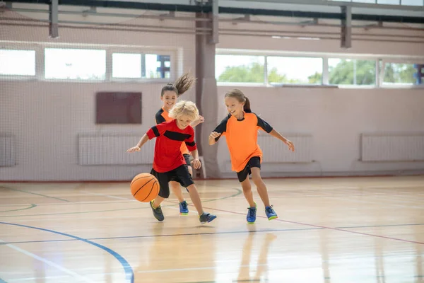 Dzieci w jasnej odzieży sportowej grające razem w koszykówkę i biegające — Zdjęcie stockowe