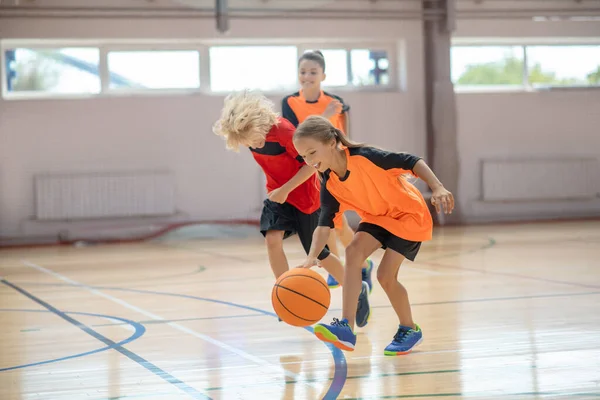 Děti v jasném sportovním oblečení hrají basketbal v tělocvičně — Stock fotografie