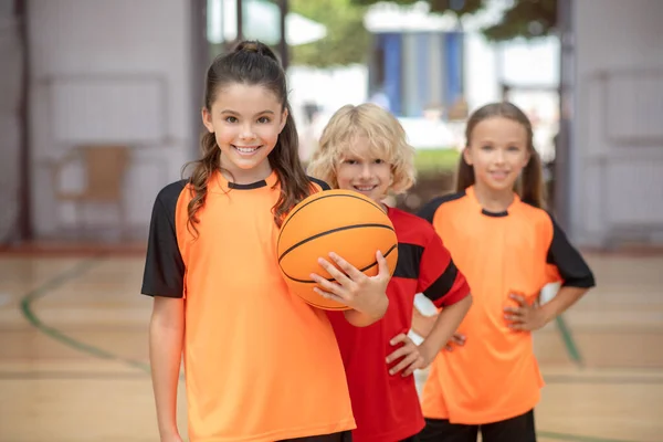 Gyerekek sportruházatban állnak egy labdával és mosolyognak. — Stock Fotó